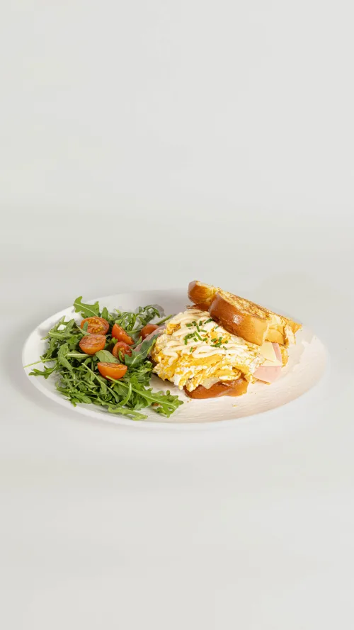 Sandwich Koreano con huevo y jamón sobre plato blanco con rugula y tomates cherry