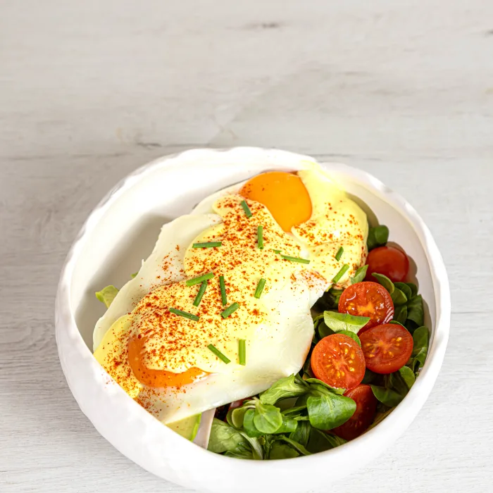 Tosta Benedict con huevo, salsa holandésa y tomates cherry en bowl blanco sobre mesa de madera clara